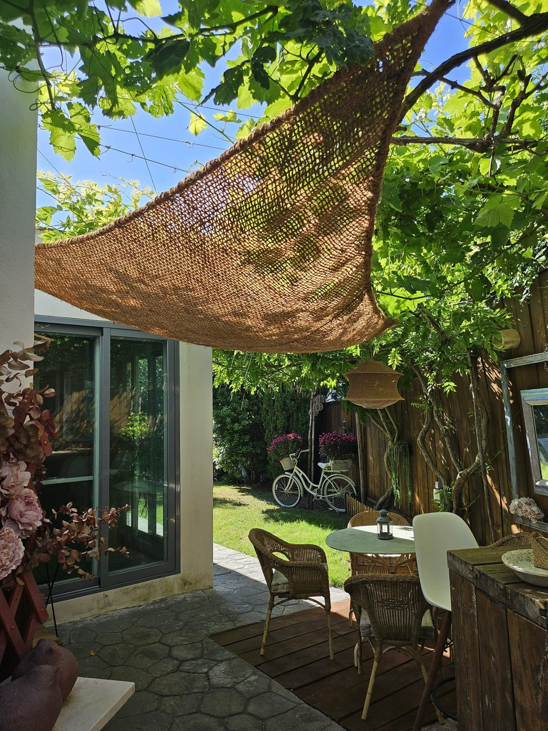 Vela de sombra triangular de fibra de coco en un jardín con vegetación