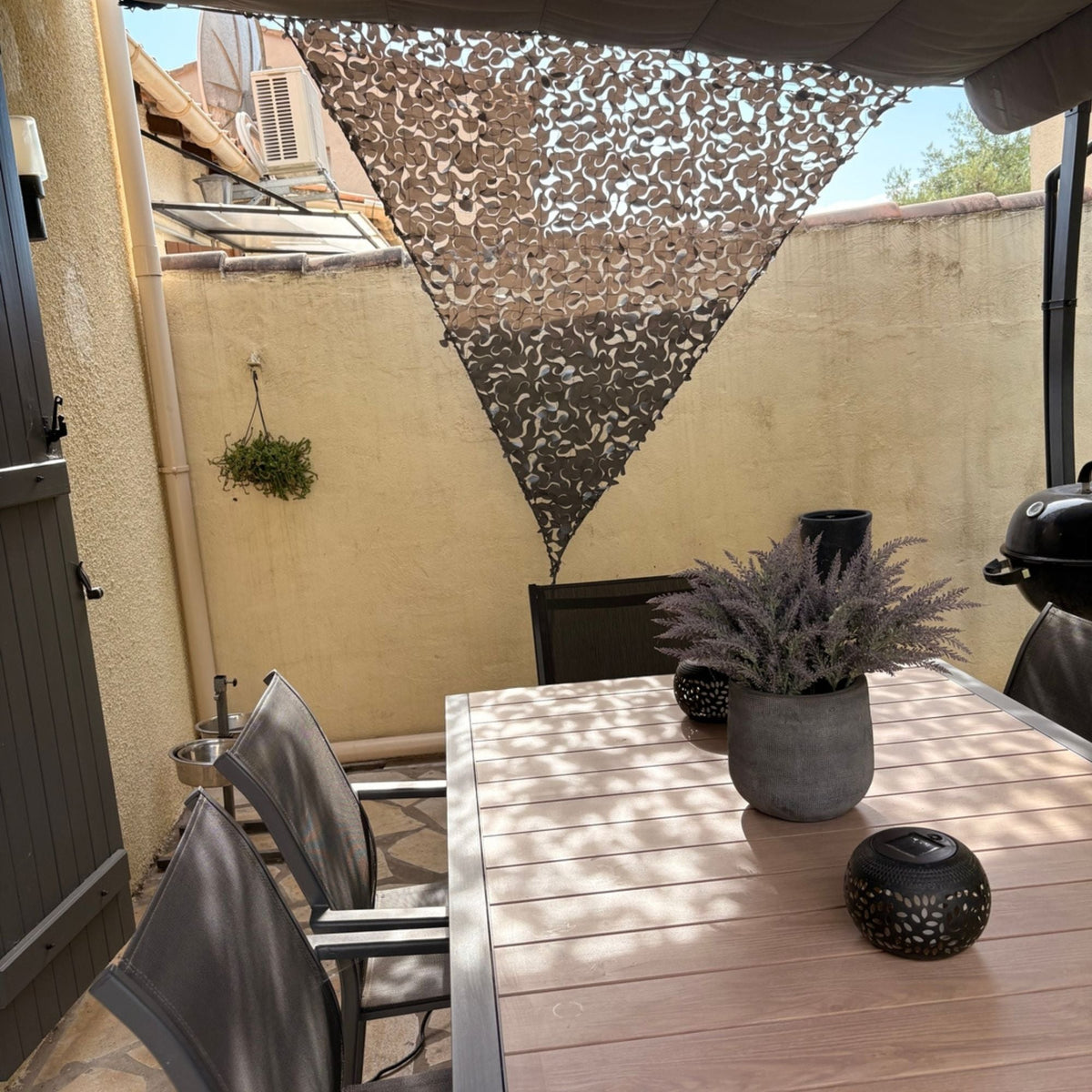 Red de camuflaje triangular gris como toldo sobre una mesa de terraza