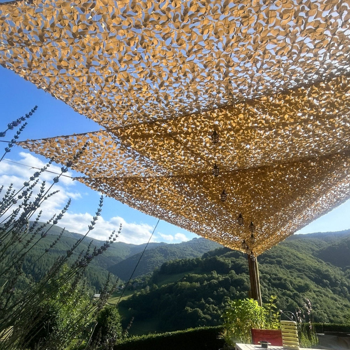 Redes de camuflaje triangulares beige sobre una terraza con vistas a la montaña