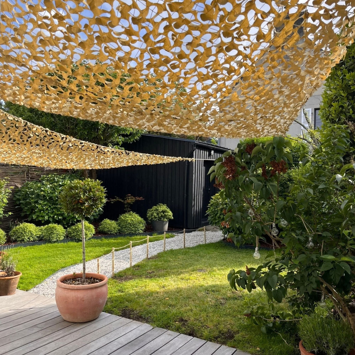 Redes de camuflaje triangulares beige como toldos en un jardín