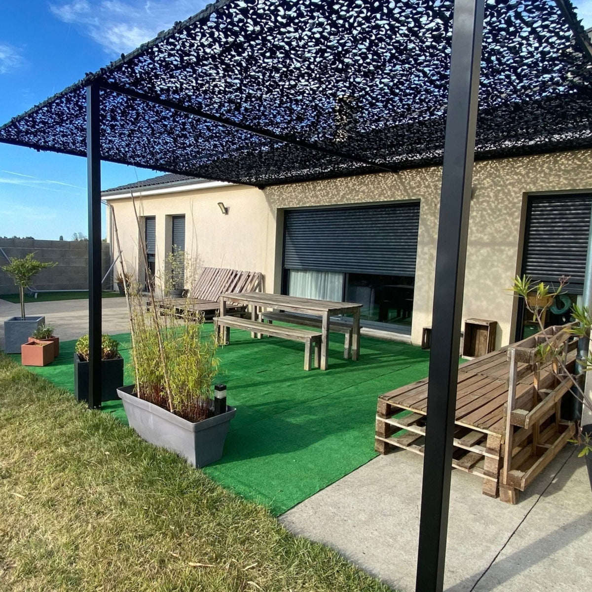 Red de camuflaje negra sobre una pérgola en una terraza con césped