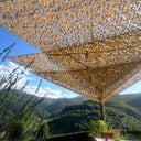 Redes de camuflaje triangulares beige sobre una terraza con vistas a la montaña